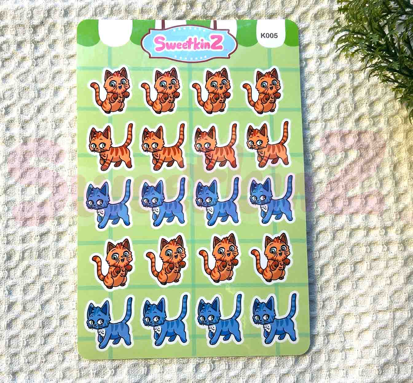 Sheet of cat-themed stickers with 'SweetkinZ' branding on a textured surface.