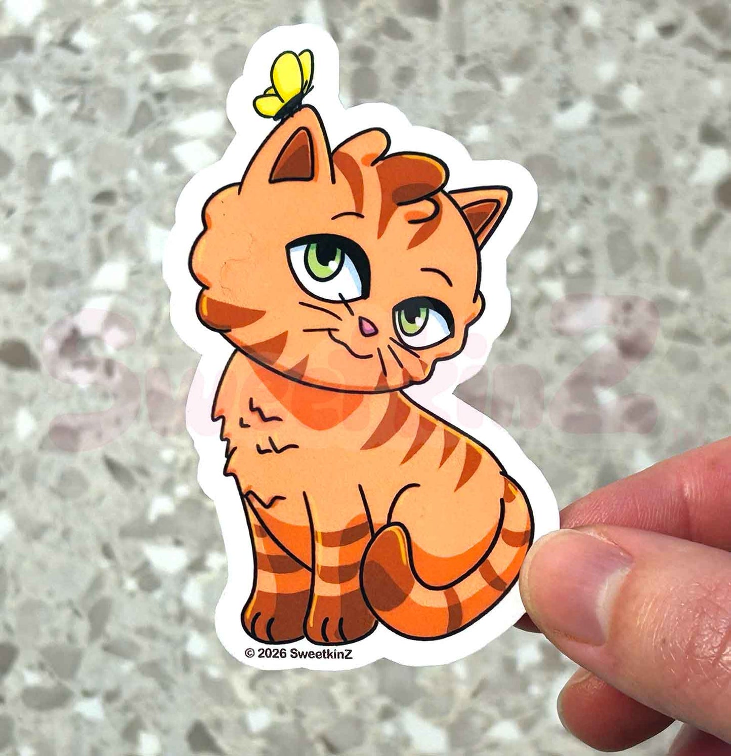 Cartoon cat sticker with a butterfly on a person's hand against a gray background