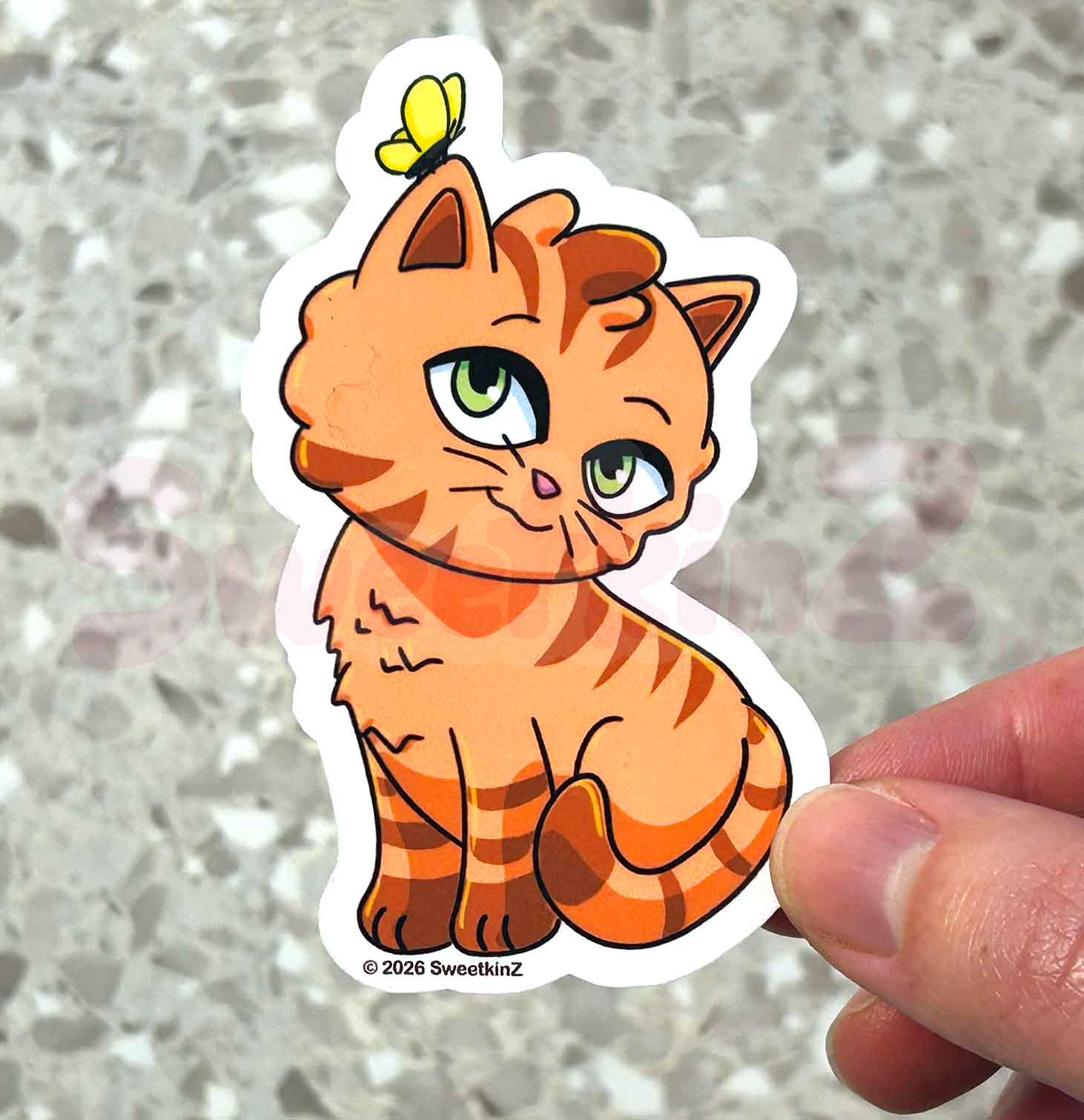 Cartoon cat sticker with a butterfly on a person's hand against a gray background